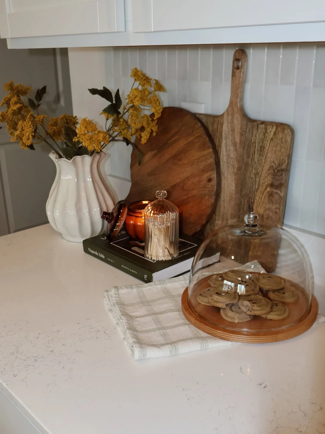 Kitchen counter styled with florals, a candle and cookies under a cloche