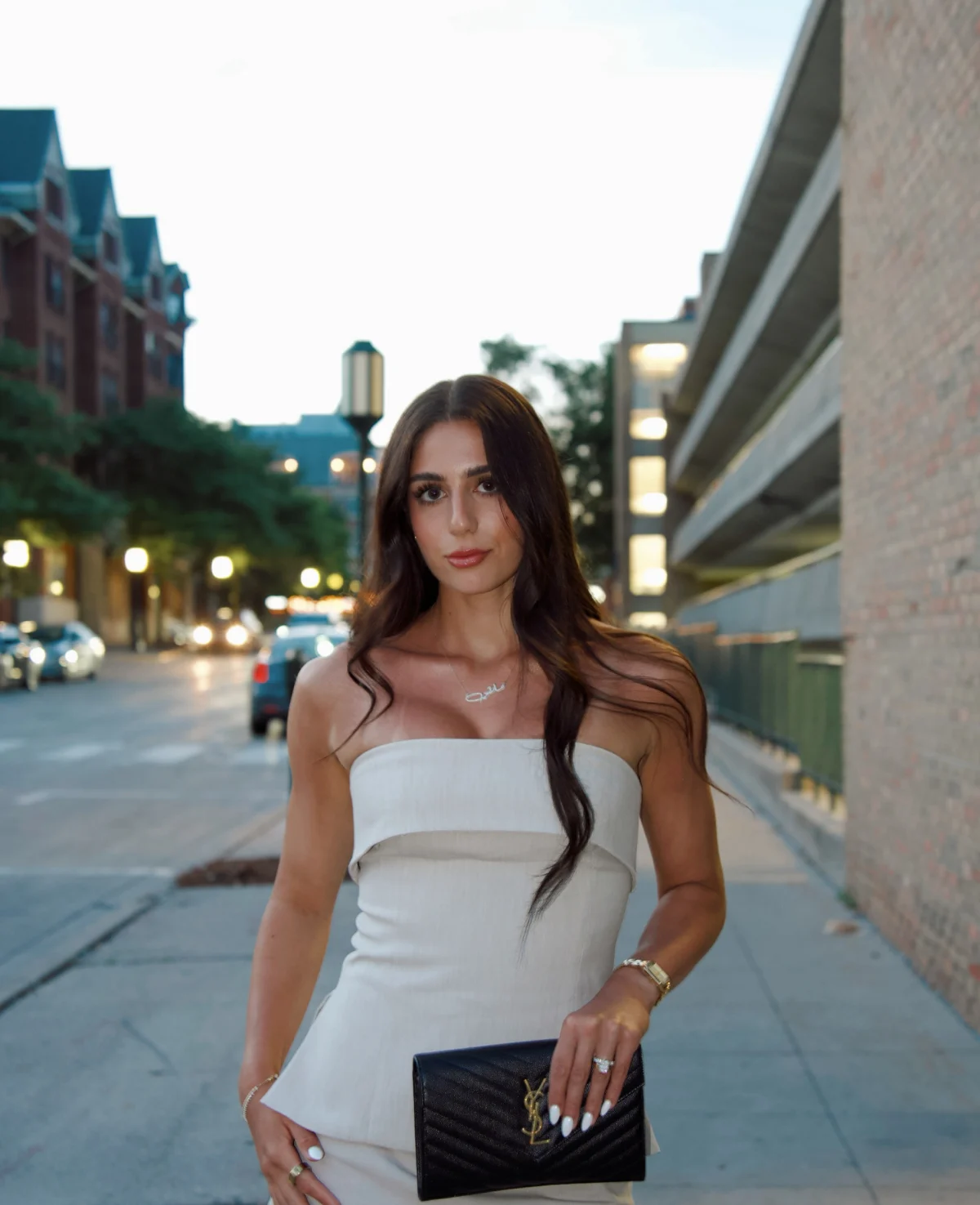 Samantha Banoub in a cream strapless dress on a city street at dusk